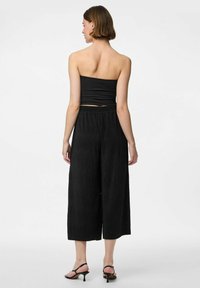 Svart bandeau-top med rynkad textur, kombinerad med högmidjade svarta culottbyxor med lös passform och subtila veck.