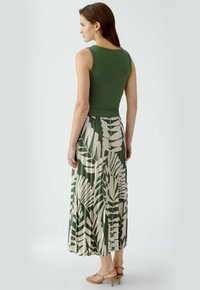 Haut olive sans manches associé à une jupe longue fluide ornée d'un motif de feuilles vertes et crème. Texture lisse avec taille cintrée.