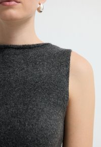 Szara wełniana bluzka bez rękawów z wysokim kołnierzem, charakteryzująca się teksturowaną powierzchnią i eleganckim, prostym wzornictwem. Widoczna metalowa kolczyk.