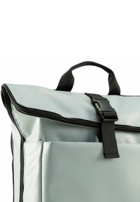 Zaino impermeabile grigio con pattina pieghevole, chiusura a zip nera e tasca frontale. Dotato di una maniglia superiore resistente e tracolla regolabile.