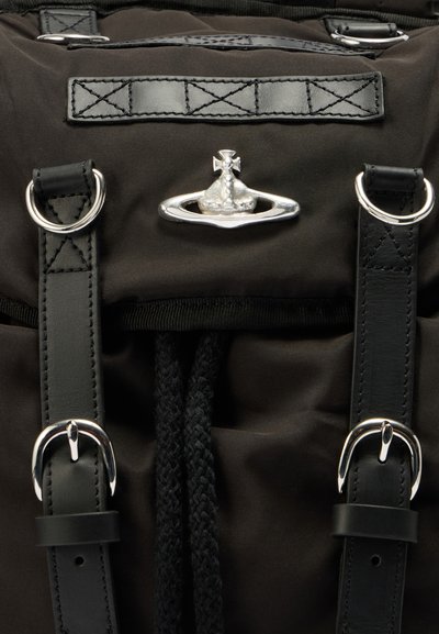 Μαύρο ύφασμα σακίδιο πλάτης με ασημί μεταλλικά εξαρτήματα, δερμάτινα λουριά και πλεκτό κορδόνι σύσφιξης. Περιλαμβάνει ένα χαρακτηριστικό μεταλλικό έμβλημα.