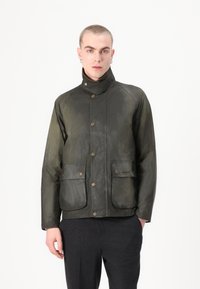 Casaco encerado verde-oliva com dois bolsos frontais, botões de latão, gola alta e uma superfície texturizada. Design slim e moderno.