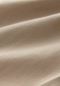 Tela beige texturizada con una superficie suave y un sutil patrón de estrías diagonales, mostrando suaves pliegues y una caída natural.