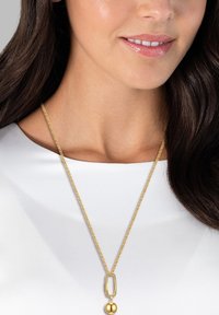 Guldhalsband med en texturerad oval länk och en polerad sfärisk hängande, vilande på en slät vit topp.