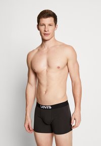 Schwarze Boxershorts mit einem breiten elastischen Levi's Bund, die eine enganliegende Passform bieten. Das Model steht vor einem hellen Hintergrund und präsentiert das Design.
