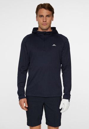 Chemise à manches longues à capuche bleu marine avec fermeture à demi-zip, arborant un petit logo blanc sur la poitrine. Tissu léger au toucher doux.