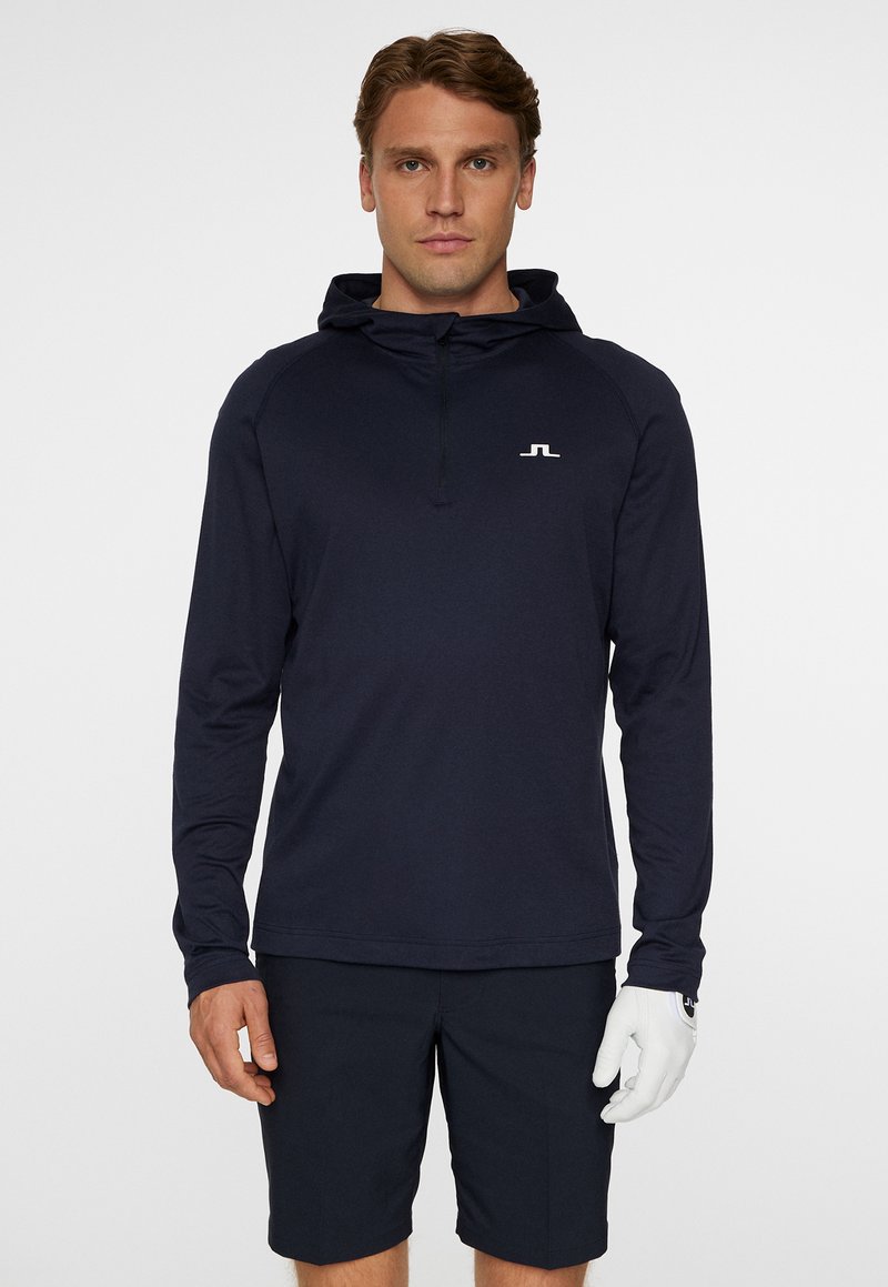 Marinblå långärmad huvtröja med halvmatchande dragkedja, prydd med en liten vit logotyp på bröstet. Lätt material med en slät yta.