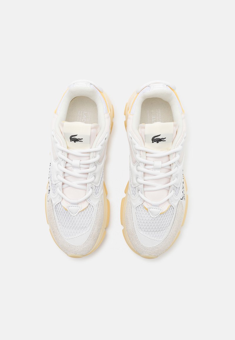 Zapatillas deportivas blancas con materiales de malla y ante, que cuentan con un diseño texturizado, suelas de goma amarillas y acentos de logo negro.