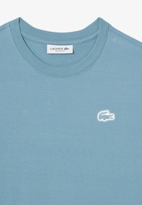 T-shirt di cotone azzurro chiaro con scollo rotondo e maniche corte. Presenta un piccolo logo di coccodrillo ricamato in bianco sul petto.