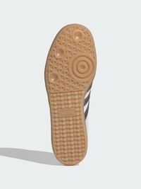 Semelle de chaussure avec une bande de roulement en caoutchouc couleur fauve présentant des motifs circulaires et géométriques et le logo Adidas embossé au centre.