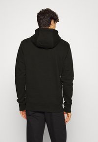 Sudadera negra de tejido suave, con una gran capucha, puños y dobladillo acanalados. El diseño es simple y minimalista, sin adornos.
