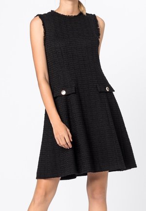 Robe noire sans manches texturée avec une jupe évasée et deux poches avant à rabat avec des boutons ronds en argent.