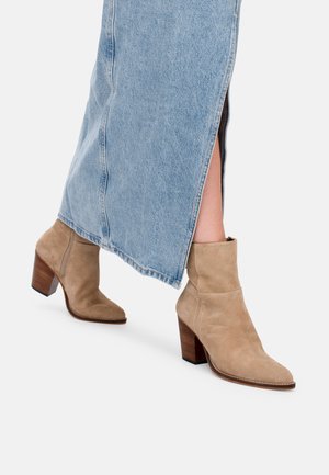Botas de ante color topo hasta el tobillo con punta afilada y un tacón de bloque de madera de 3 pulgadas, combinadas con una falda de mezclilla azul clara que presenta una abertura lateral.