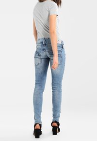 Světlomodré úzké džíny s vybledlým praním, pěti kapsami a podrobným prošíváním. Svázané s šedým tričkem a černými robustními podpatky.