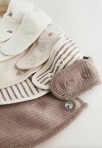 Soft cotton bibs in cream and brown tones, featuring ribbed texture, striped patterns, and snap closures for adjustable fit.