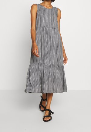 Sleeveless midi dress with black diamond pattern, tiered skirt, worn with black ankle-strap sandals on a person against white background.
