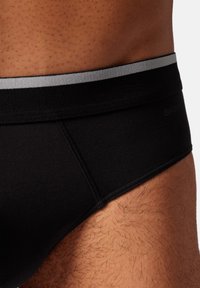 Schwarze Baumwollslips mit einem grauen elastischen Bund und flachen Nähten, die eine enge Passform und glatte Textur betonen.