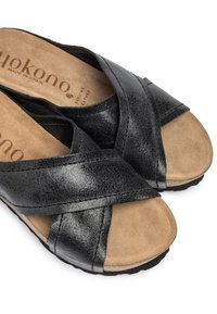 Sandales en cuir noir avec un design à brides croisées, bout ouvert et semelle intérieure en suédine douce sur une semelle en caoutchouc texturée. Fabriquées en Espagne.