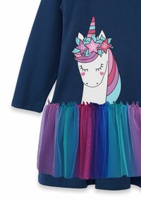 Långärmad klänning i marinblått med ett unicorntryck, som har en flerfärgad tullkjol i nyanser av lila, blått och rosa.