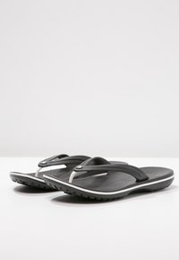 Svarta flip-flops med strukturerad fotbädd, som har en mjuk rem, silverdetalj och vit kant längs sulan. Hållbar gummisula.