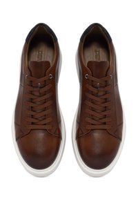 Sneakers in pelle marrone con accenti testurizzati, suole bianche e lacci marroni. Presentano un colletto imbottito e dettagli cuciti lungo i lati.