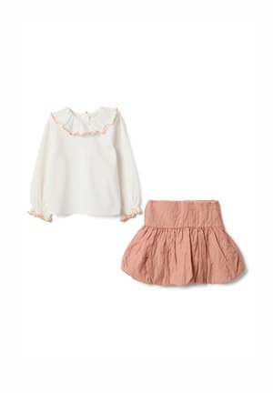 Blusa blanca de manga larga con cuello y puños con volantes bordeados en durazno, combinada con una falda plisada texturizada de color durazno.