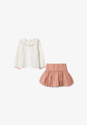 Weißbluse mit langen Ärmeln, mit Rüschen am Kragen und an den Bündchen in Pfirsich abgesetzt, kombiniert mit einem texturierten, plissierten Rock in Pfirsichfarbe.