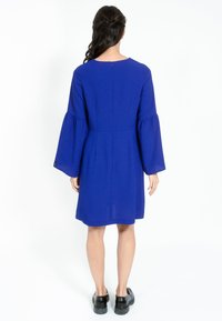 Rochie albastră, până la genunchi, cu mâneci largi, în formă de clopot și decolteu rotund. Confecționată dintr-un material neted, cu închidere la spate.