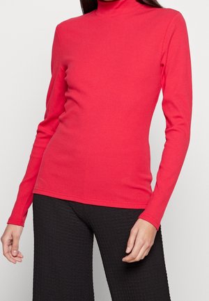 Rotes geripptes Langarm-Turtleneck-Oberteil mit enganliegender Passform und glatter Textur. Kombiniert mit schwarzen strukturierten weiten Hosen.