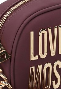 Borsa in finta pelle color mogano con forma arrotondata, caratterizzata da lettering e accessori in oro lucido. Chiusura con zip e dettaglio in catena visibili.