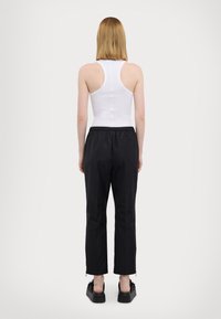 Weißes, enges Tanktop mit einem Racerback-Design, kombiniert mit schwarzen Hosen. Die Hosen haben einen elastischen Bund und seitliche Schlitze am Saum.
