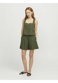 Conjunto de dos piezas de lino verde que incluye un top de escote cuadrado y pantalones cortos holgados con cinturilla fruncida. Sandalias negras de punta abierta.