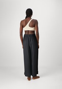 Top corto asimétrico beige de un solo hombro con tejido texturizado acompañado de pantalones anchos de tiro alto en negro; cinturilla elástica, acabado suave, sin patrones.