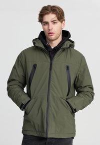 Giubbotto imbottito verde oliva con cappuccio, dotato di tasche sul petto con zip, cerniere nere a contrasto e polsini a coste. Texture liscia.