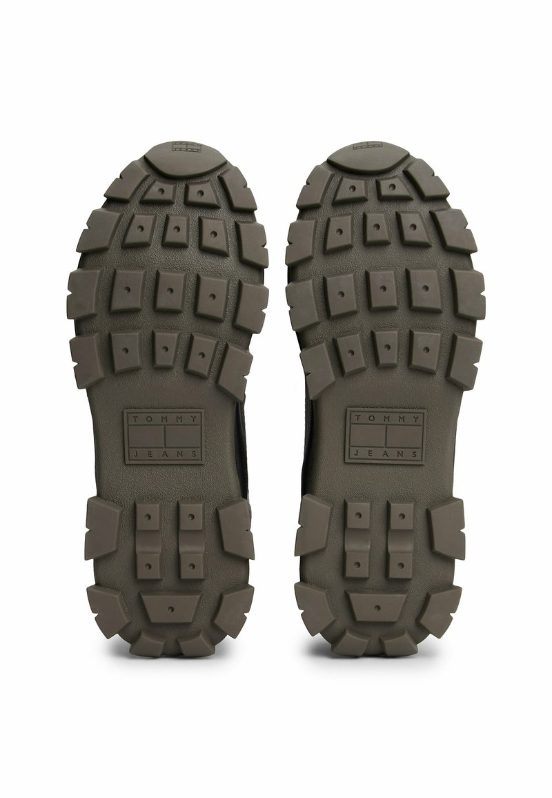 Schwarze Gummisohle mit robustem Design, die ausgeprägte Profile und ein rechteckiges "TOMMY JEANS"-Logo in der Mitte aufweist.