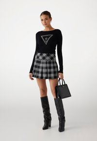Schwarzes Langarmshirt mit einem dreieckigen Logo, schwarzer und weißer karierter Minirock, knielange schwarze Stiefel und eine kleine schwarze Handtasche.