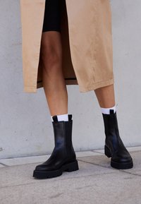 Schwarze Lederstiefeletten mit einer klobigen Sohle und einer weichen Textur. Mit elastischen Seitenpaneelen und kontrastierenden Laschen an der Hinterseite.