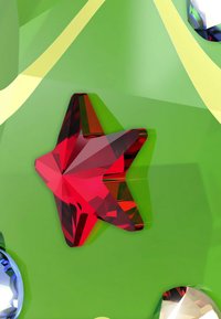 Czerwony kryształ w kształcie gwiazdy na gładkiej zielonej powierzchni o refleksyjnej fakturze, z dwoma dodatkowymi kolorowymi akcentami z kamieni szlachetnych.