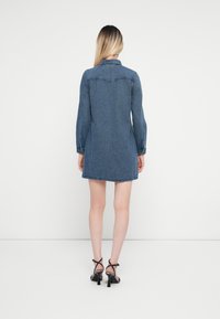 Denim kleita ar garām piedurknēm, ar apkakles kakla izgriezumu un nedaudz izplestu apakšdaļu. Mugurpusē ir yoke un divi pogu akcenti, kas apvienoti ar melniem papēžiem.