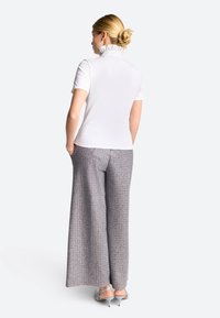 Weißes kurzärmliges Hemd mit rüschendem Kragen, kombiniert mit weit geschnittenen, gemusterten Hosen in Blau und Beige, die aus einem strukturierten Stoff bestehen.