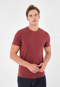 Bordeauxrotes T-Shirt mit kurzen Ärmeln aus glattem Stoff, mit Rundhalsausschnitt und normaler Passform, kombiniert mit dunkelblauen Jeans.