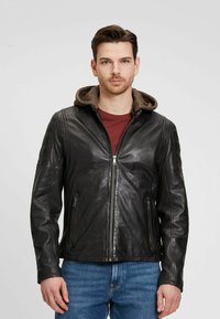 Chaqueta de cuero negra con capucha forrada de forro polar marrón, cierre frontal con cremallera y dos bolsillos laterales con cremallera. Textura suave con sutiles detalles de costura.