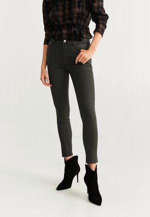 Kvinde iført mørke skinny jeans, sorte højhælede ankelstøvler og en mørk ternet langærmet top med flæsekant.