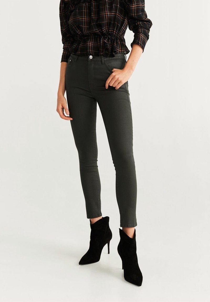 Femme portant un jean skinny foncé, des bottines noires à talons hauts et un haut à manches longues à carreaux foncés avec un ourlet à volants.