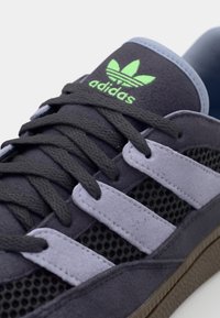 Tmavošedé semišové tenisky majú syntetické pruhy v purpurovej farbe, sieťkovú výplň a zelené logo Adidas na jazyku. Gumová podrážka.