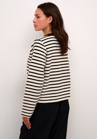 Pulover rayat în crem și negru, cu guler rotund, mâneci lungi și tricot texturat. Spatele este ușor scurtat la tiv.