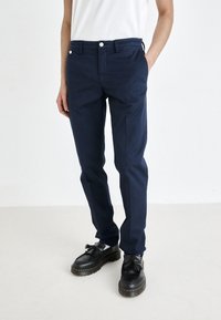 Navy blue cotton trousers with a straight-leg design, front pockets, button closure, and belt loops, styled with black shoes.
