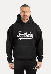 Sudadera negra con capucha hecha de una mezcla de algodón, que presenta un logo blanco de "Smilodox", un bolsillo canguro y puños de canalé. Combinada con pantalones negros a juego.