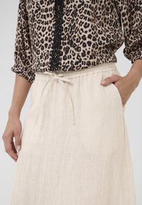 Bluză cu imprimeu de leopard, cu detalii cu nasturi, asociată cu o fustă ușoară, de culoare ivorie, cu șnur în talie, care are buzunare laterale și un finisaj texturat.