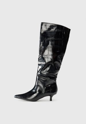 Schwarze knielange Stiefel aus glänzendem, krokodilgeprägtem Material, mit spitzem Zeh und niedrigem Kitten-Absatz. Glatte Textur mit sanften Falten.